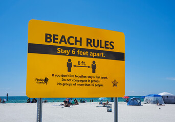 A prominent yellow sign illustrating the Beach Rules of social distancing to stay six feet apart. Clearwater Beach, FLorida, USA.