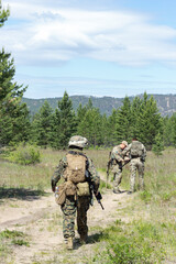 Group of fully armed american soldiers on the summer forest road on military range, active military game airsoft.