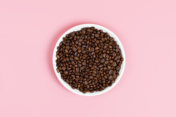 Fragrant coffee beans on a white plate on a pink background. Coffee shop or store concept. Top view, minimalism.