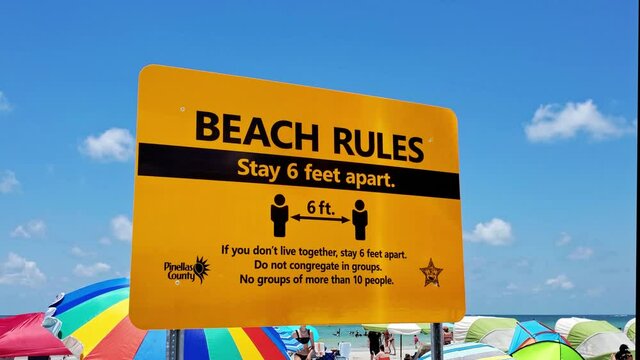 A prominent yellow sign illustrating the Beach Rules of social distancing to stay six feet apart. Clearwater Beach, FLorida, USA.