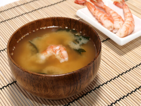 Miso soup with shrimp in a Japanese wooden bowl on a bamboo mat