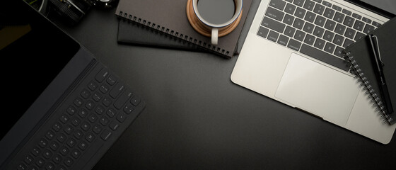 Dark modern workspace with digital tablet, laptop, coffee cup, schedule books and copy space