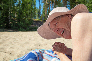 Shy Old Woman +80, in a summer hat and a swimsuit on the beach. Smiles. Sunny, summer day by the sea. Concept: healthy lifestyle, relaxation