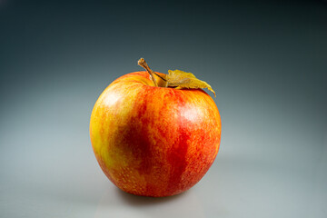 Red apple with a dry leaf on a dark background.