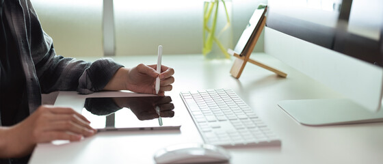 Female entrepreneur using digital tablet with stylus on white office desk with computer and decoration