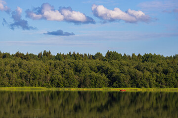 Beautiful forest lake. Red boat in the distance. Outdoor recreation and fishing on the lake. Summer travel and vacation in the countryside.