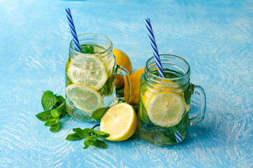 Summer refreshing detox cocktail. Water with lemon, mint and ice in mason jar on white blue background. Rustic style.
