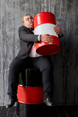 fat caucasian businessman is inseparable from the oil business, he hugs oil barrel and looks at...