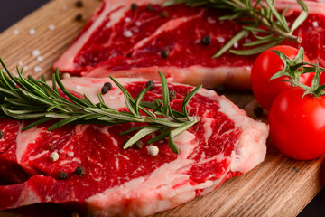 Fresh raw beef steak on wooden cutting board over black background with spices, top view.
