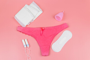 Women's panties with menstrual cups, sanitary pads and tampons on pastel pink background. Top view. Concept of critical days, menstruation, feminine hygiene
