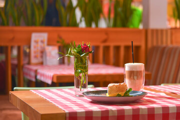 Piece of cream lemon meringue pie served with Latte coffee on a table with red plaid tablecloth.