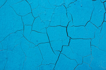 The old cracked blue paint on a wall surface. Peeling paint on wall seamless texture. Pattern of rustic blue grunge material. Vintage pattern from cracks, chips, stains for print and design.