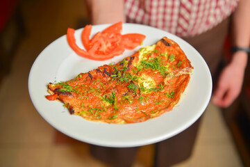 Waiter is holding a plate with traditional breakfast, omelette with tomatoes and fresh dill. Focus on plate.