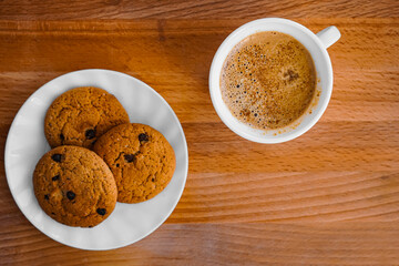 Oatmeal cookies on a plate on a table with a wooden texture and a cup of coffee