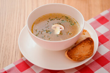 Chicken soup with vegetables and meat served in a white bowl over rustic wooden background with red plaid tablecloth.
