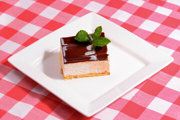 Slice of New York Cheesecake with chocolate and mint on white plate on plaid background in a restaurant. Sweet dessert