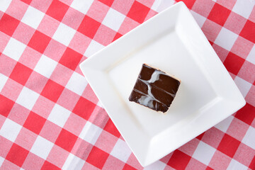Chocolate souffle with thick chocolate ganache glaze served on a white plate on red plaid background