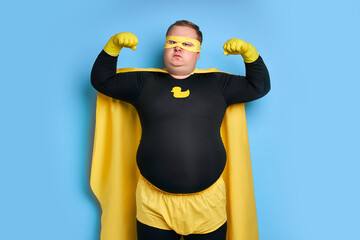 comical caucasian superhero with arrogant face isolated over blue background. man shows his...