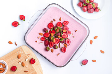 Top view of delicious creamy berry souffle cake in a glass dish with strawberries and almonds on a white table