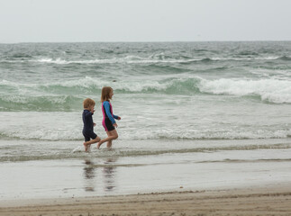 Two children, a 4 year old boy and a 6 year old girl, running along the waves at a beach from a distance