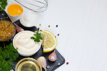 Bowl of mayonnaise sauce next to ingredints for making homemade sauces