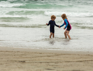 Two young children, four and six years old, a boy and a girl, holding hands and running through the waves at the beach