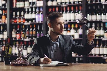Man sommelier is holding glass of wine and tasting transparency light sediments in restaurant