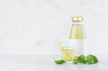 Fresh vegetable green spinach juice in glass bottle with blank label mock up with glass, straw, leaves in soft light white interior on wood table.