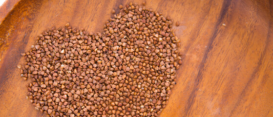 Theme of diet and weight loss on a white background. buckwheat in a wooden plate is laid out in the shape of a heart.