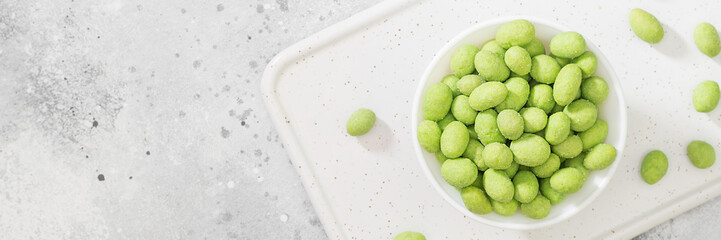 Fried peanuts in wasabi in a white bowl on a light gray table. Banner with space for text
