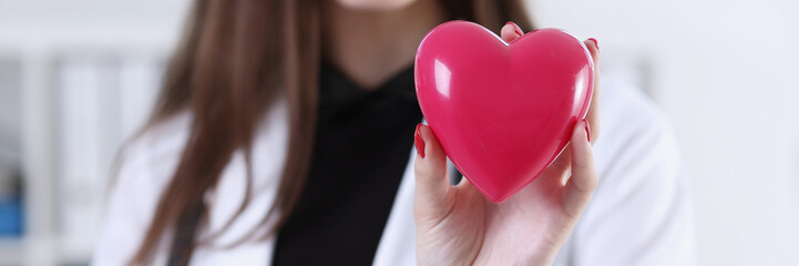 Female medicine doctor hands holding and covering red toy heart closeup. Cardio therapeutist,...