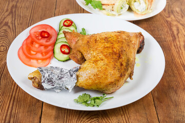 Fried chicken leg with vegetables on rustic table close-up