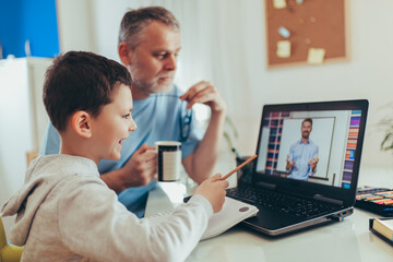 Obraz premium Schoolboy educate online. Father helps his son with home work. Boy in video conference with teacher on laptop at home.
