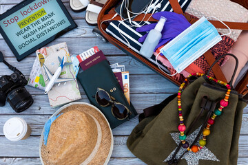 Above view of travel female accessories, luggage and personal items, camera, maps and boarding pass, facial mask due to coronavirus on wooden background - concept of travel safe
