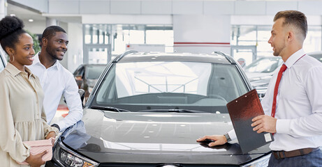 beautiful black afro couple attentively listen to consultant in dealership, confident salesman...