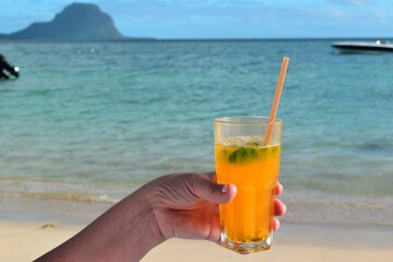 Fresh tropical juice in hand with beautiful beach background. Vacations, holidays, sun, beach.