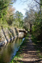 Old irrigation canal in Provence. Small stone bridges cross the canal. A footpath runs along the canal.