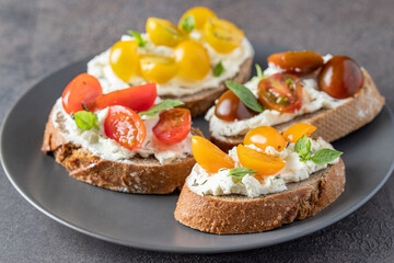 Delicious crusty bread slices with cream cheese and different tomato cherry  garnished with fresh basil leaves on the table .Appetizer bruschetta or snack