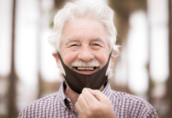 Portrait of smiling senior man with white hair wearing facial mask due to coronavirus - new normal concept, palm trees and nobody else