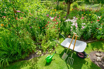   Schubkarre mit Gartenwerkzeug vor den Blumenbeeten