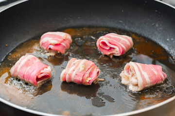 Raw rolls with bacon are fried in a pan. Cooking junk and fatty foods.
