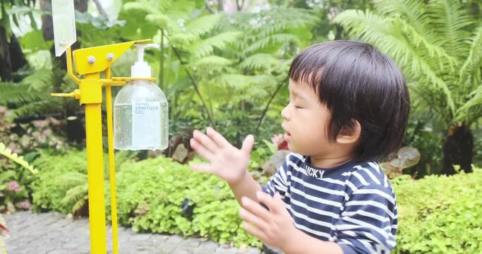 Toddler asian child boy using Alcohol spray jel bottle in his hand for prevent Corona virus or Covid-19 disease in park. Washing and cleaning hand by Alcohol gel.