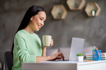 Profile side photo of smart chinese girl ceo expert sit desk work remote laptop texting typing report hold beverage mug in house indoors