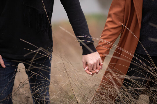 The couple holds hands against the background of the field, the hands of a guy and a girl, love, together forever, beautiful body parts
