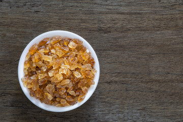 Natural organic brown crystal rock sugar in white ceramic cup over old wooden background.