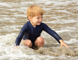 Young boy, four years old, running and playing at the beach. Blonde hair and navy swimming suit, smiling and laughing.