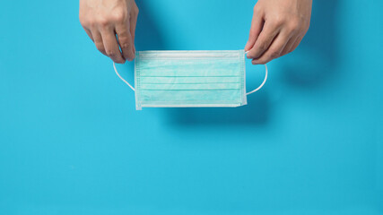 The hand is hold face Mask or surgical mask on blue background.