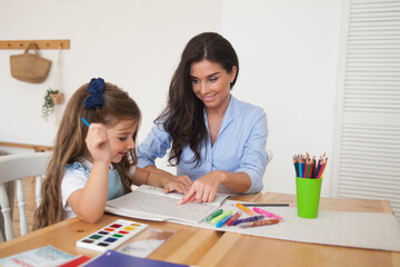 Smiling mother and daughter preparing for lessons and draws at the table with pencils and paints. Parent and pupil of preschool. First day of fall autumn. Girl from elementary class, back to school