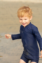 Young boy, four years old, running and playing at the beach. Blonde hair and navy swimming suit, smiling and laughing.