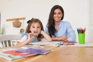 Smiling mother and daughter preparing for lessons and draws at the table with pencils and paints. Parent and pupil of preschool. First day of fall autumn. Girl from elementary class, back to school